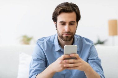 Akıllı telefon kullanan, kulaklık takan, koltukta oturan ciddi bir adam.