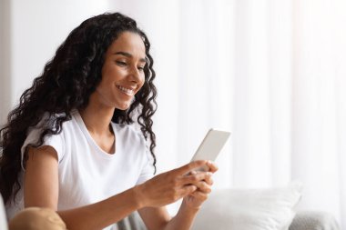 Akıllı telefon kullanan ve evde gülümseyen genç bir kadın.