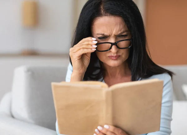 Senior zavarodott nő szemüvegben próbál könyvet olvasni — Stock Fotó
