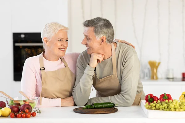 Los cónyuges mayores abrazan la preparación de la cena de pie en la cocina moderna —  Fotos de Stock