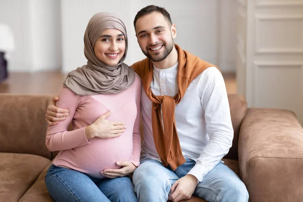 Feliz musulmán marido abrazando embarazada esposa sentado en casa — Foto de Stock