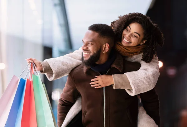 Black man piggybacking his woman looking at mall window — Stock Photo, Image