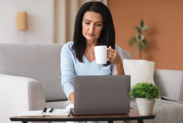 Reife Frau sitzt auf Sofa und trinkt Kaffee — Stockfoto