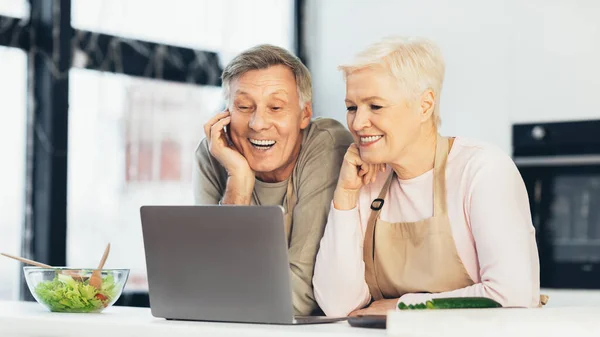 Ältere Ehepartner sitzen am Laptop in der modernen Küche zu Hause — Stockfoto