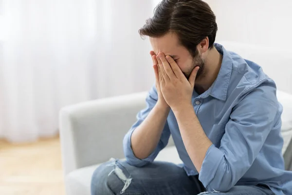 Απογοητευμένος άνθρωπος κλαίει καλύπτοντας το πρόσωπο κάθεται στον καναπέ στο σπίτι — Φωτογραφία Αρχείου