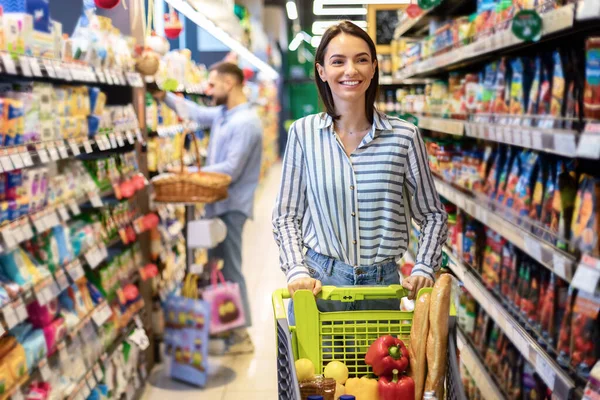 Wanita muda bertopeng dengan keranjang belanja di supermarket — Stok Foto