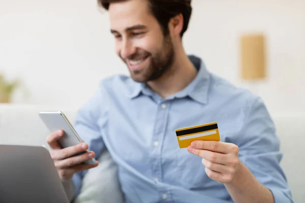 Chico alegre de compras con teléfono celular y tarjeta de crédito en casa — Foto de Stock