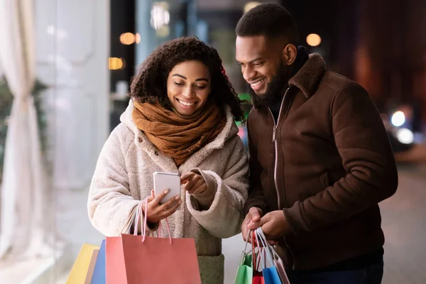 Feliz pareja afro usando teléfono inteligente con muchas bolsas de compras —  Fotos de Stock