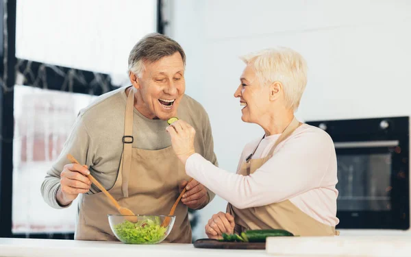 Senior Family Couple Feeding Each Other Cooking Dinner In Kitchen