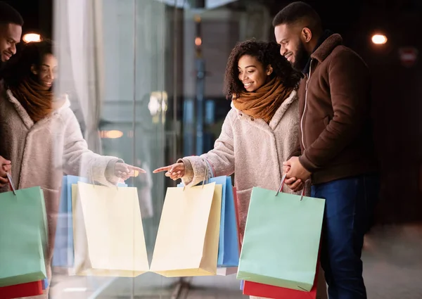 Happy black family with shopping bags pointing at mall window — Stock Photo, Image