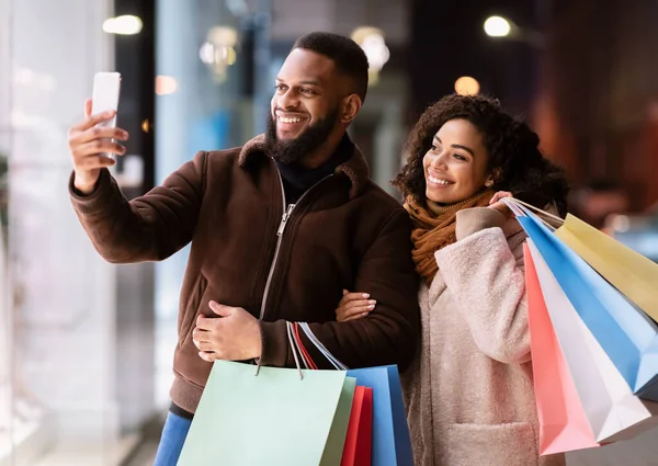 Feliz pareja afro tomando selfie después de ir de compras en el centro comercial —  Fotos de Stock