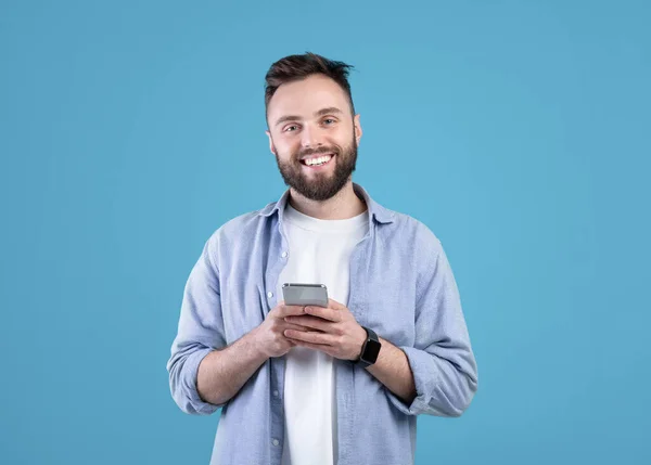 Retrato de cara barbudo legal usando telefone celular no fundo do estúdio azul — Fotografia de Stock