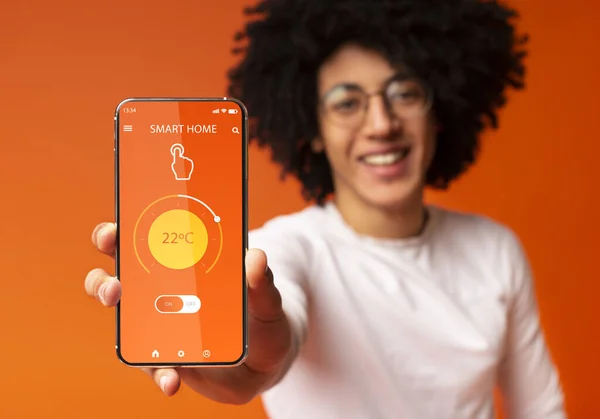 Κολάζ με μαύρο άνδρα που δείχνει απομακρυσμένο σύστημα ελέγχου smart home στην οθόνη του κινητού τηλεφώνου, πορτοκαλί φόντο — Φωτογραφία Αρχείου