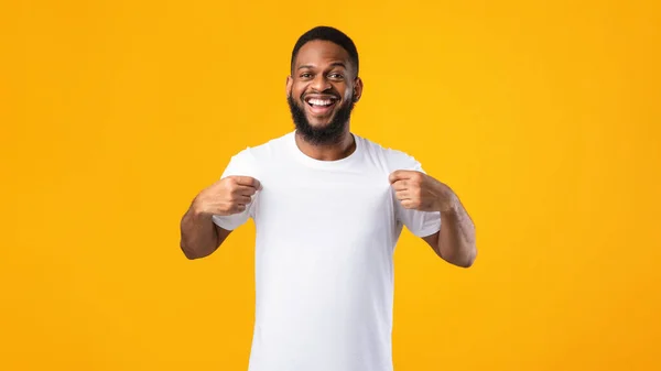 Alegre hombre negro mostrando su camiseta blanca sobre fondo amarillo — Foto de Stock