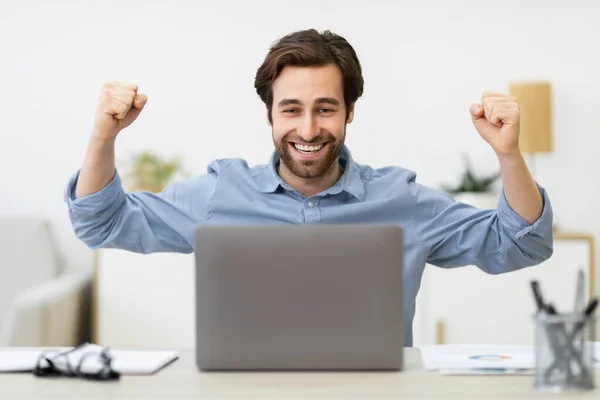 Empresario alegre en el ordenador portátil celebrando el éxito empresarial sentado en la oficina — Foto de Stock