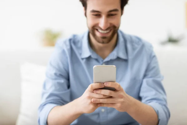 Chico feliz usando mensajes de texto para teléfonos inteligentes sentado en el sofá en casa —  Fotos de Stock