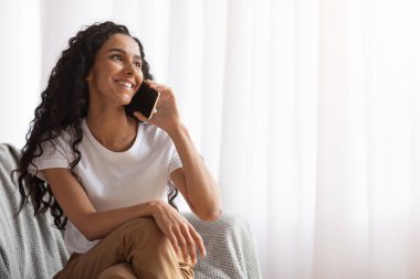 Pencerenin kenarında oturan mutlu genç bayan, cep telefonuyla konuşuyor.