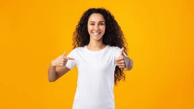 Stüdyoda kendini parmağıyla işaret eden neşeli bir kadın var.