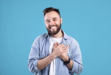 Milenyum adamı elini göğsüne koyup mavi stüdyo arka planında olumlu duygular ve minnettarlığını dile getiriyor.