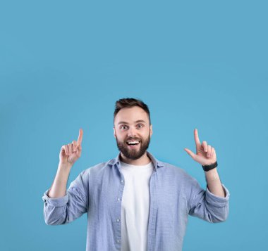 Heyecanlı sakallı adam mavi stüdyo arka planındaki boşluğu işaret ediyor.