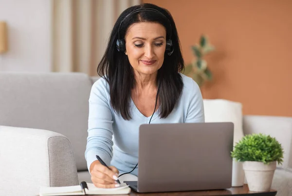 Mature woman in headset writing and using computer at home