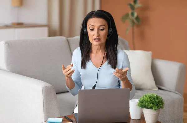 Mature woman in headset having video call on computer — Stock Photo, Image