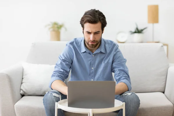 Man fronsen met behulp van laptop met problemen zitten op de bank binnen — Stockfoto