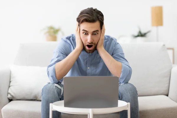 Потрясенный бизнесмен на ноутбуке трогает голову, имея проблемы сидя в помещении — стоковое фото