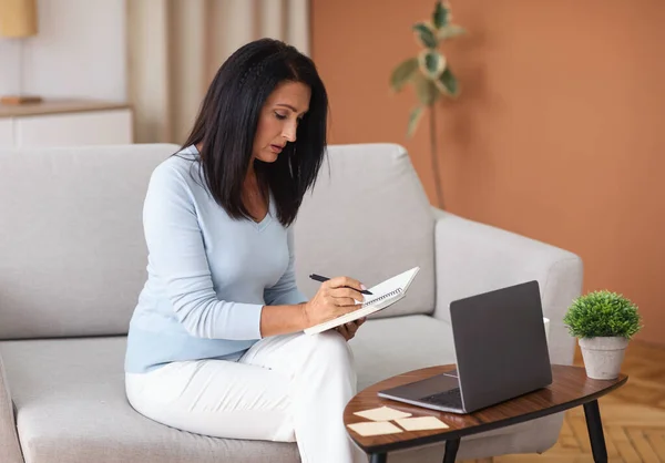 Donna matura che scrive nel notebook e utilizza il computer portatile a casa — Foto Stock