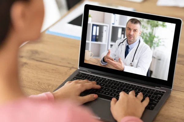 Неузнаваемая пациентка, имеющая онлайн видео-звонок с врачом на ноутбуке, в помещении — стоковое фото