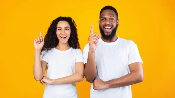 Vielrassiges Paar zeigt mit erhobenem Zeigefinger auf gelbem Hintergrund — Stockfoto