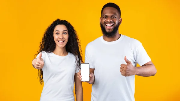 Vzrušený pár Zobrazení telefonu obrazovka gesta palce nahoru přes žluté pozadí — Stock fotografie