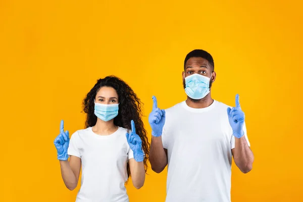 Paar dragen van maskers en handschoenen Wijzen vingers omhoog, gele achtergrond — Stockfoto