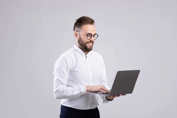 Усміхнений молодий хлопець в офісному одязі використовує ноутбук на сірому фоні студії — стокове фото