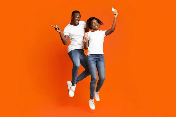 Homem e mulher afro-americanos felizes fazendo selfie enquanto saltam — Fotografia de Stock