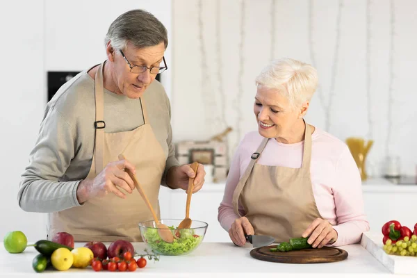 Los cónyuges mayores preparan ensalada de verduras saludables para la cena en la cocina —  Fotos de Stock