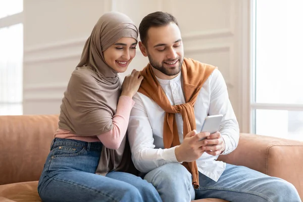 Junges muslimisches Paar sitzt mit Handy auf Couch im Haus — Stockfoto