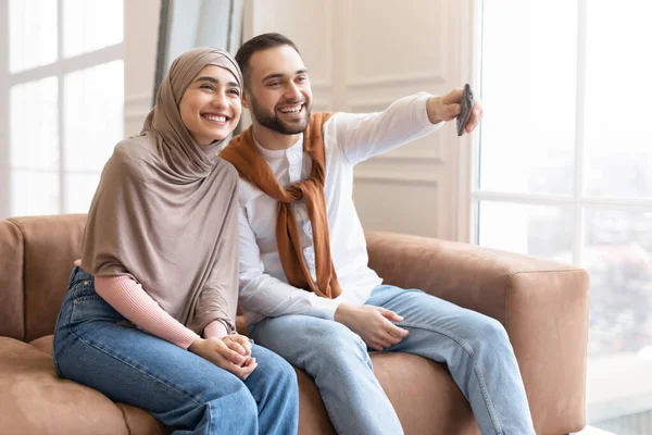 Casal muçulmano feliz assistindo TV sentado no sofá em casa — Fotografia de Stock