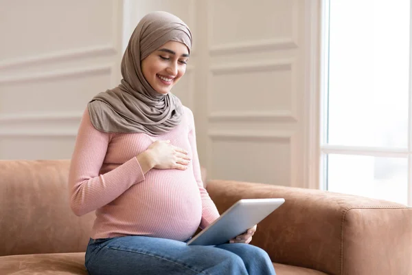 Radostné těhotné muslimské Lady pomocí digitální tablety sedí doma — Stock fotografie