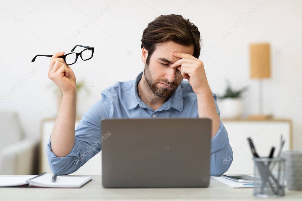 Tired Man At Laptop Massaging Nosebridge Holding Eyeglasses In Office