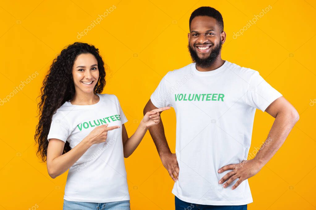 Woman Volunteer Pointing Fingers At Male Colleague Over Yellow Background