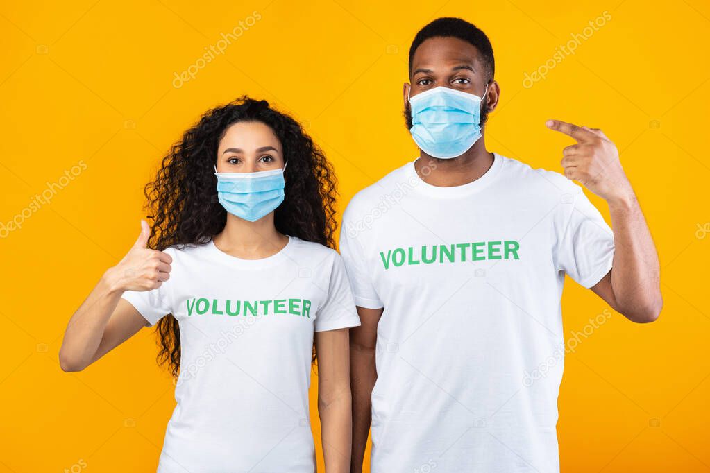 Volunteers Pointing Fingers At Masks Gesturing Thumbs-Up Over Yellow Background