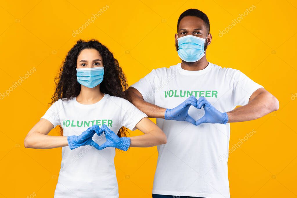 Two Volunteers Gesturing Heart-Shape Wearing Masks And Gloves, Yellow Background