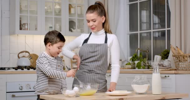Kleiner Junge rührt Teig in Glasschüssel, Mutter schaut ihn an, genießt Zeit miteinander in der Küche, Zeitlupe — Stockvideo