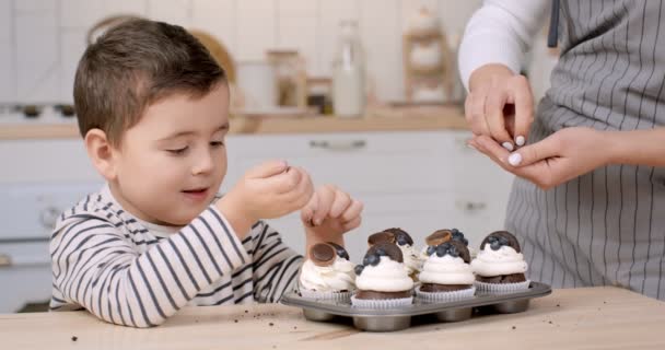 Niedliche kleine Junge helfen seine Mutter zu dekorieren hausgemachte Cupcakes in der Küche, Nahaufnahme — Stockvideo