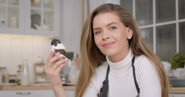 Close-up portret van jonge mooie vrouw banketbakker poseren met zelfgemaakte gedecoreerde cupcake in de keuken — Stockvideo