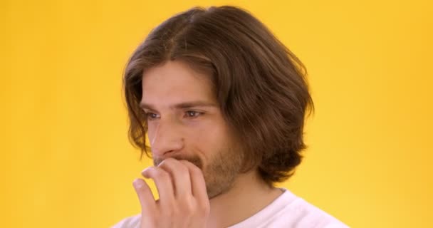 Close up retrato de jovem homem tímido sentindo-se confuso, olhando incerteza para a câmera, cobrindo a boca, fundo laranja — Vídeo de Stock