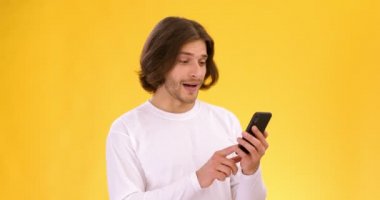 Genç adam cep telefonuna bakıyor, sosyal medyada geziniyor, haberleri seyrediyor, sarı stüdyo geçmişi, yavaş çekim.