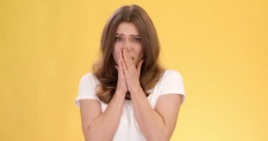 Yüzünü saklayan korkmuş genç bir kadının portresi, korku ve iğrenme duygusu, turuncu stüdyo geçmişi, yavaş çekim.