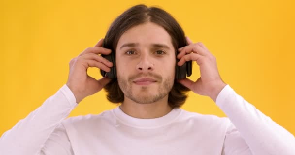 Молодий чоловік у нових бездротових навушниках і насолоджується чудовим звуком, танцює над помаранчевим студійним фоном — стокове відео